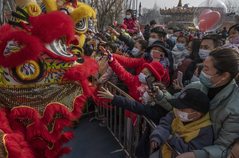 People wearing face masks reach towards a team performing a traditional lion dance to mark the first day of the Lunar New Year at a park in Beijing, Feb. 12, 2021. Kevin Frayer/Getty Images/People Visual