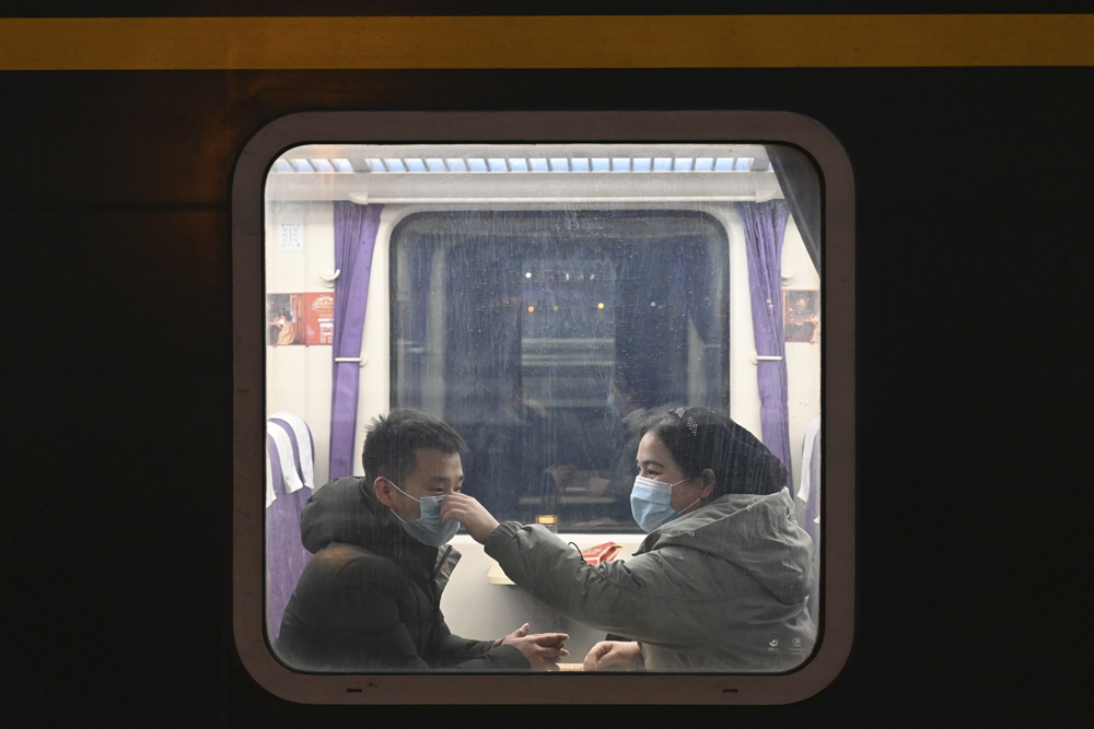 A woman helps her husband put on a face mask properly on a homeward-bound train at a railway station in Shijiazhuang, Hebei province, Feb. 11, 2021. Zhai Yujia/CNS/People Visual