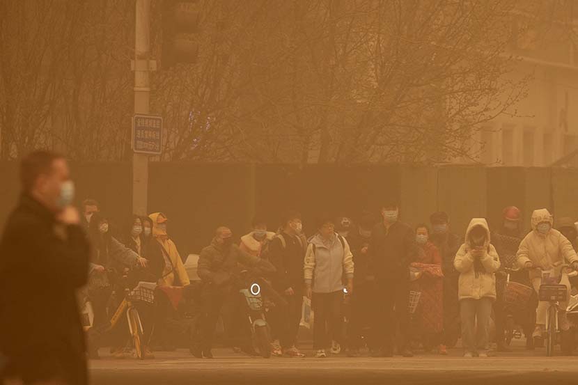 People wait to cross an intersection during the morning rush hour as a massive sandstorm engulfs Beijing, March 15, 2021. The sandstorm brought a tinted haze to Beijing’s skies and sent air quality indices soaring. People Visual