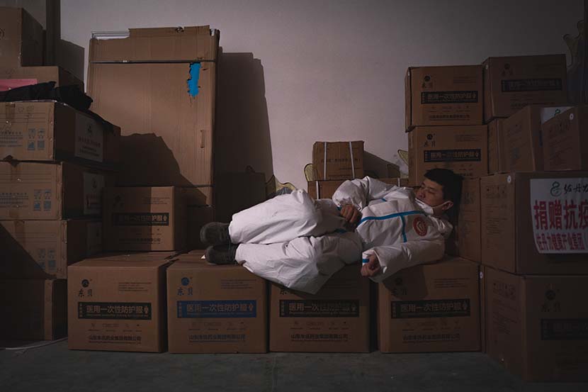 A volunteer naps atop boxes of protective gear in Tonghua, Jilin province, Feb. 2, 2021. Pan Yi for Sixth Tone