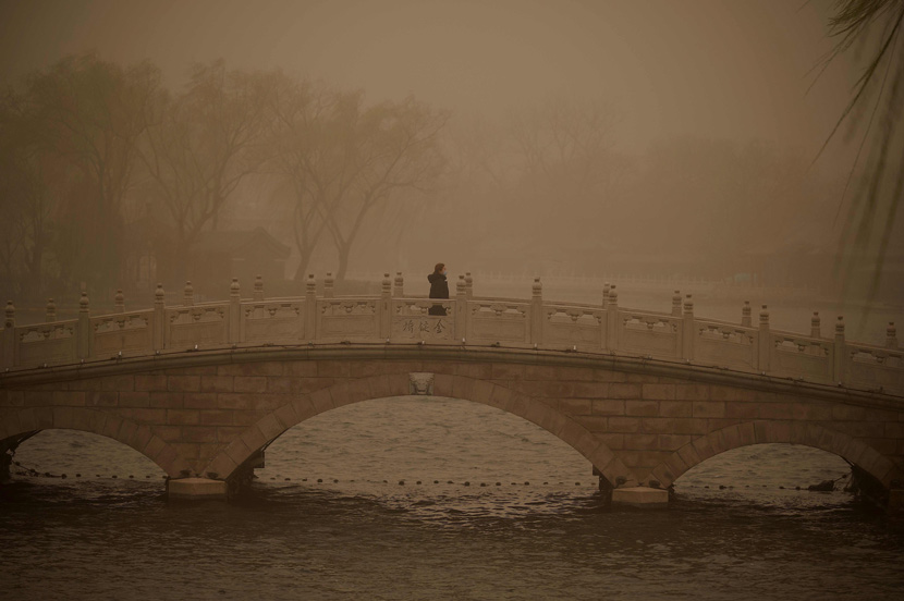 A woman crosses a bridge at a park during a sandstorm in Beijing, March 15, 2021. Noel Celis/AFP/People Visual