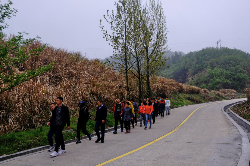 The residents hike in single file along the mountain road, accompanied by the carers, in Jinzhai County, Anhui province, March 2021. Wu Huiyuan/Sixth Tone