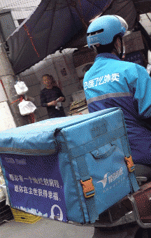A GIF shows a courier riding his scooter with a slogan on the delivery box, 2021. The slogan is from poet Hai Zi’s “Facing the Sea, With Spring Blossoms.” The text reads: “May you have a brilliant future, and may you enjoy happiness in this earthly world.” From 共治空间 on WeChat