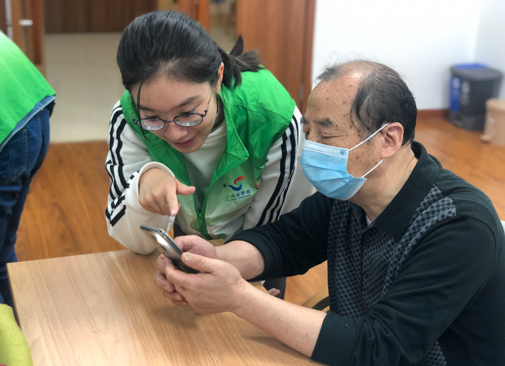 Volunteer Cai Yijun teaches a senior how to use his phone, in Shanghai, November 2020. Courtesy of Shanghai Normal University’s “Smart Elderly” program