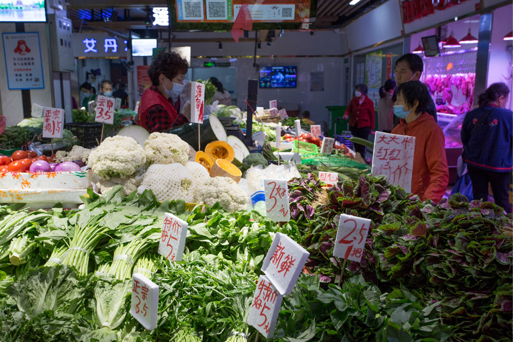 Liu Guilan (left) talks to a customer at her vegetable stall at a wet market, in Wuhan, Hubei province, April 25, 2021. Wu Peiyue for Sixth Tone