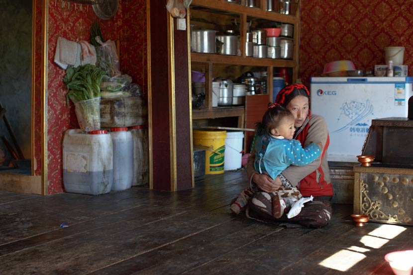 Wosar Lhamo holds her young son at home in Tagong Township, Kangding County, Sichuan province, May 9, 2017. Zhou Pinglang/Sixth Tone