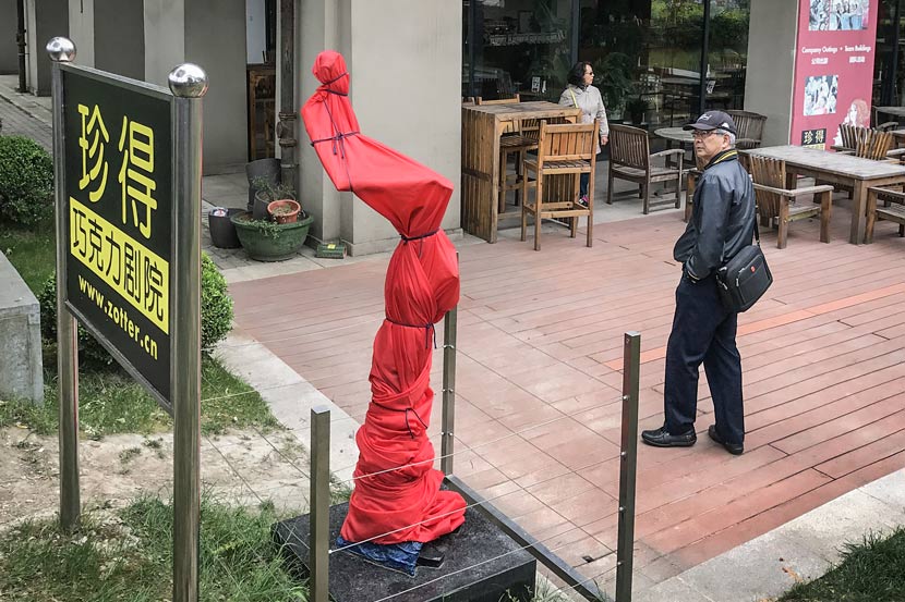A sculpture of an adult man urinating  is covered by a red tarp near the International Fashion Center in Yangpu District, Shanghai, May 3, 2017. VCG