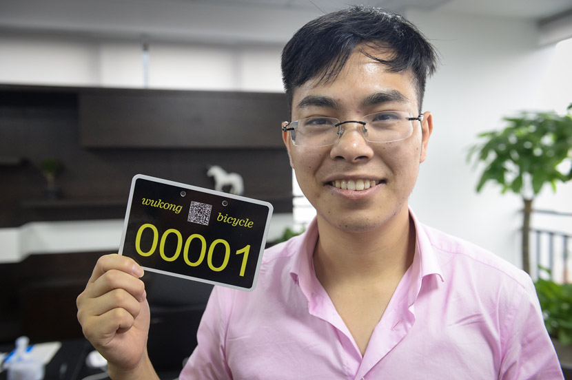 Lei Houyi holds up the first Wukong shared bike license plate at his office in Chongqing, June 19, 2017. Ren Jun/Chongqing Evening News