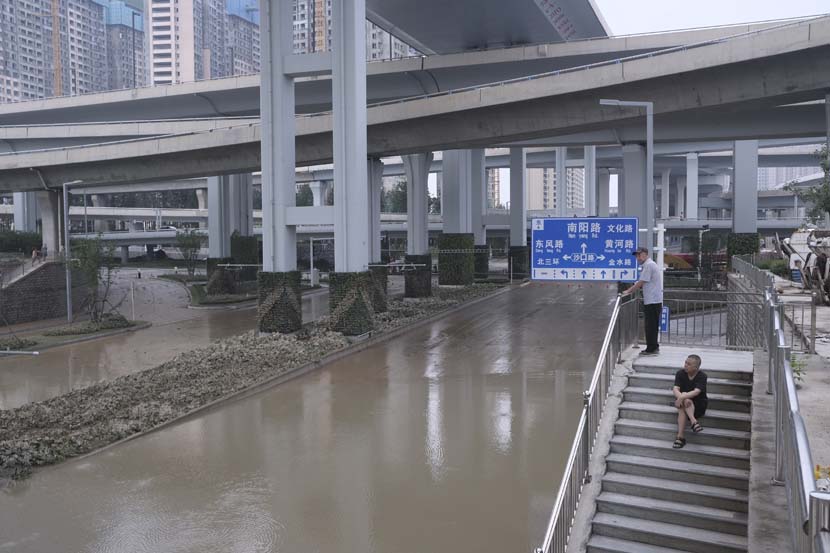 Two men look at a flooded street in Zhengzhou, Henan province, July 22, 2021. Wu Huiyuan/Sixth Tone