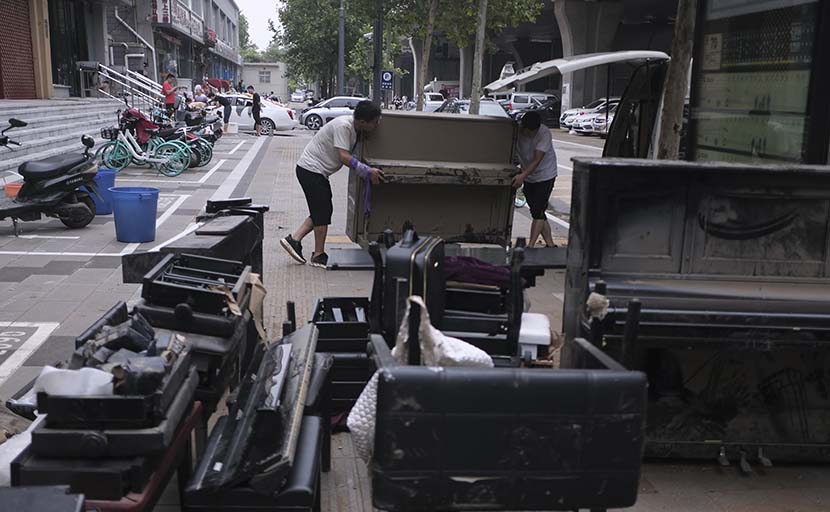 Two men move a piano out of a flooded store on Shakou Road, Zhengzhou, Henan province, July 22, 2021. Wu Huiyuan/Sixth Tone