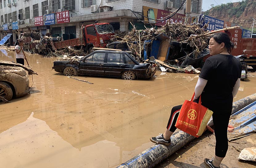 Deng Hui looks at the flooded street where her shop is located in Mihe Town, Henan province, July 24, 2021. Yuan Ye/Sixth Tone