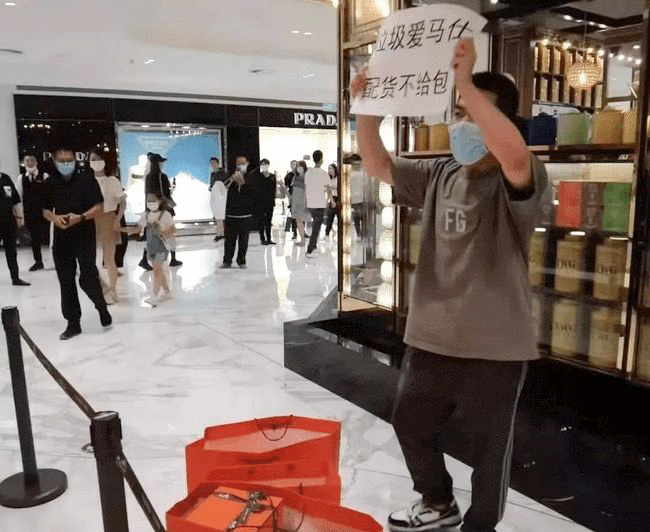 A man holds a sign saying “Rubbish Hermès — peihuo but no bag” outside a store in Beijing, July 2021. From “DZ” on Xiaohongshu