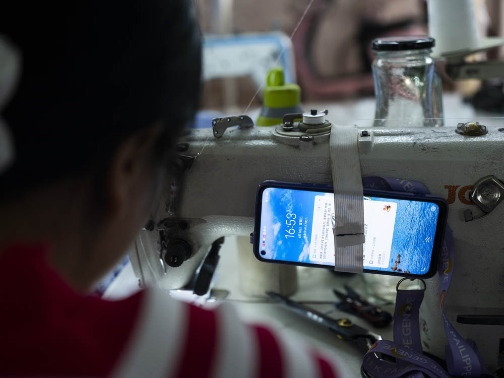 Huang Hongxia ties her phone to the sewing machine so she knows when it’s time to go pick up her son from school, June 2021. Courtesy of Lü Meng