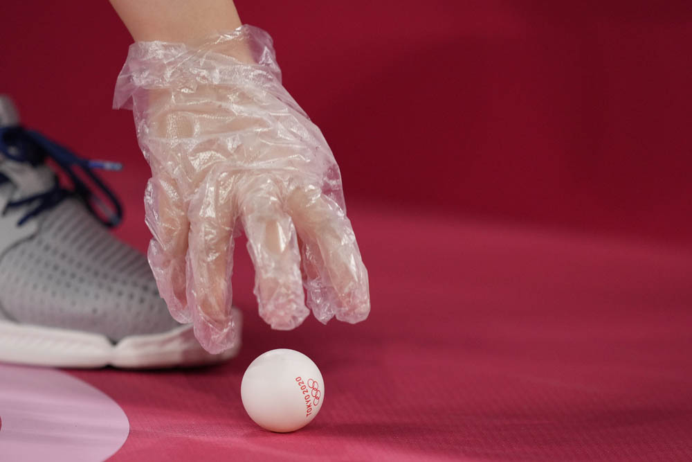 A gloved volunteer picks up a ball during the men’s table tennis event, Aug. 3, 2021. Kin Cheung via People Visual