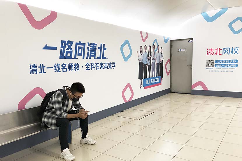 A man sits by an ad for Qingbei in Beijing, Sept. 7, 2021. People Visual