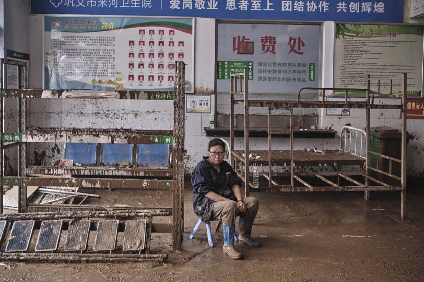 A woman sits in a flooded clinic in Mihe Town, Henan province, July 23, 2021. Wu Huiyuan/Sixth Tone