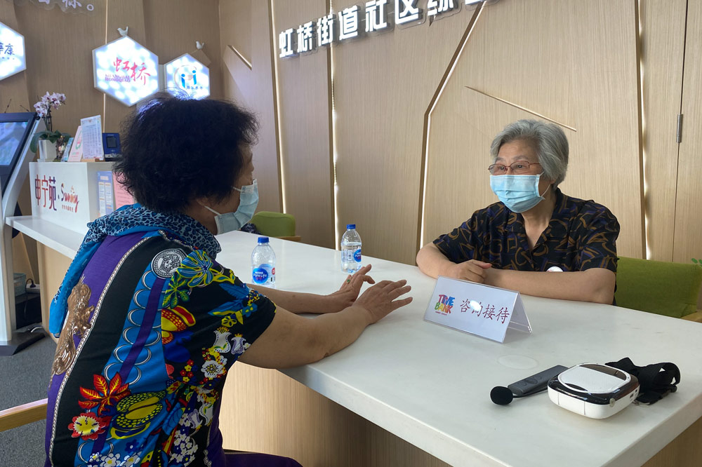 Chen Wenhua answers a local resident’s questions while working as a receptionist in Hongqiao Subdistrict, Shanghai, Aug. 19, 2021. Fan Yiying/Sixth Tone
