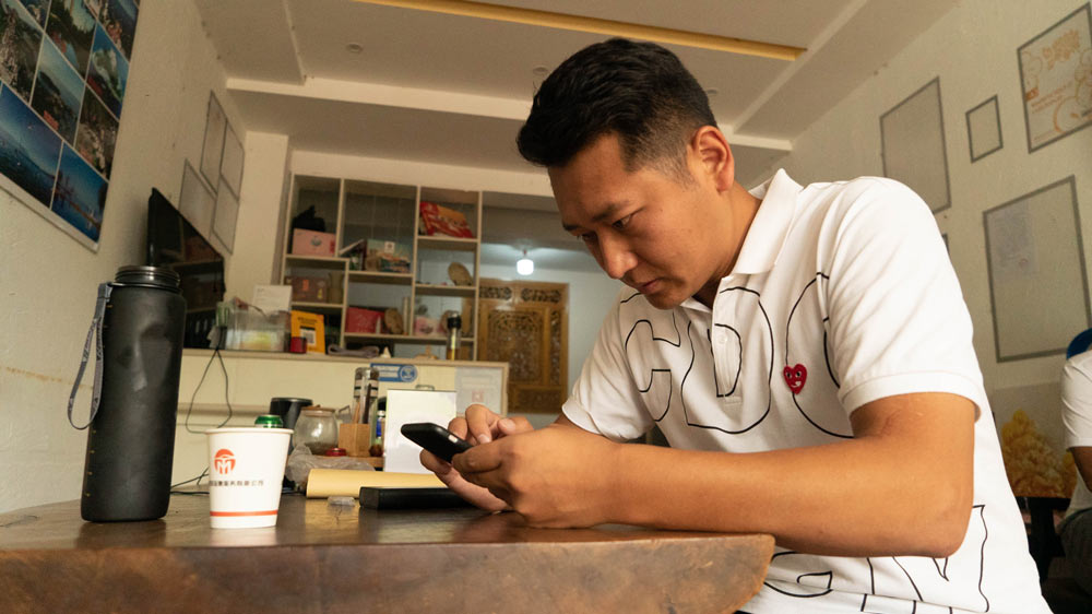You Jiang, a co-owner of car rental firm Bonnie Car Rental, checks his phone inside his shop in Dali, Yunnan province, Oct. 7, 2021. Jiang Yaling/Sixth Tone