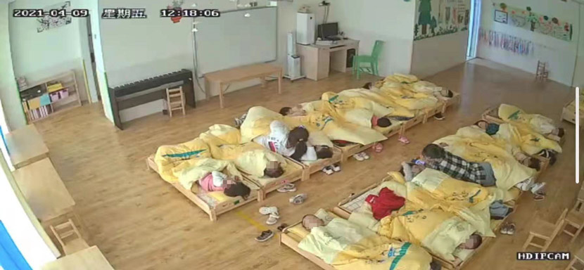 A screenshot captured by Luo shows two teachers lying in bed with students during naptime. Luo says one of the teachers was “spooning” a boy while using her phone. Courtesy of Luo Huan