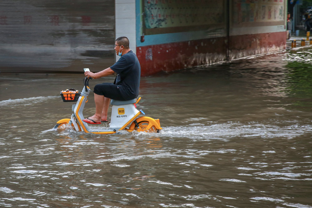 A man rides a shared e-bike through floodwaters in Xiangyang, Hubei province, July 16, 2021. Yang Dong/People Visual