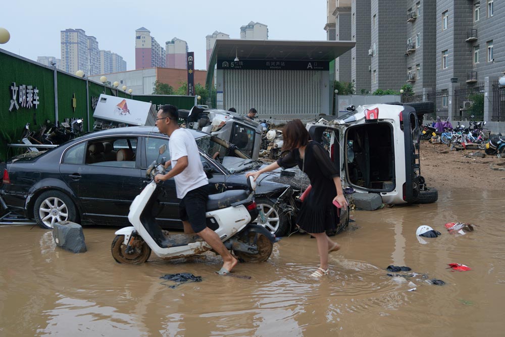 People pass by a subway station entrance on a flooded street in Zhengzhou, Henan province, July 22, 2021. People Visual