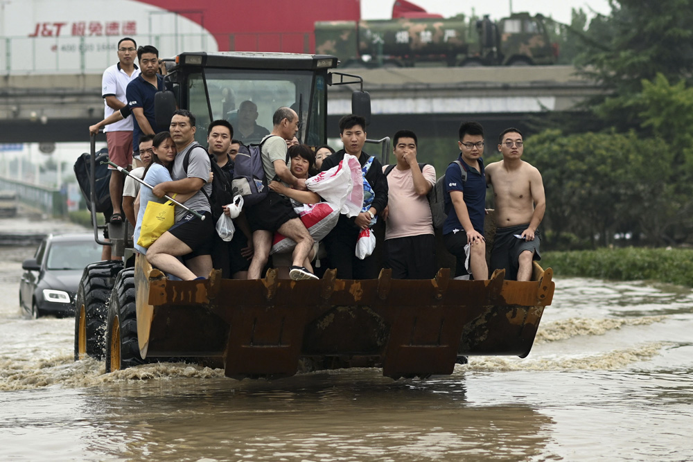 People ride in the front of a wheel loader to cross a flooded road in Zhengzhou, Henan province, July 23, 2021. Noel Celis/AFP