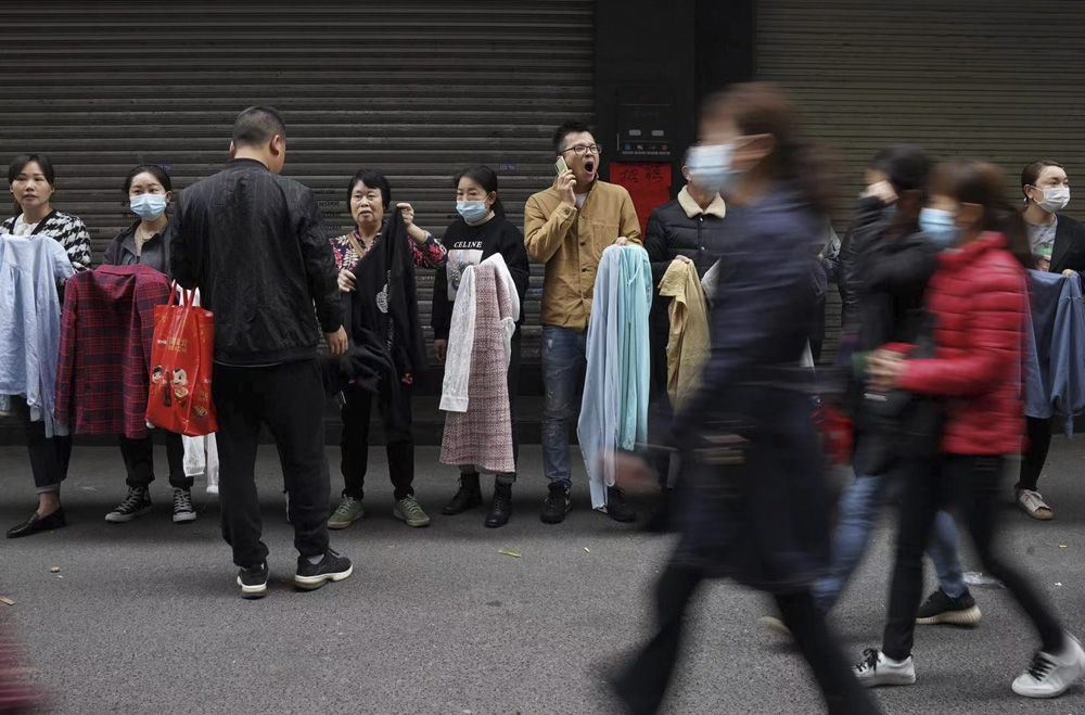 Garment factory owners stand in a line with samples in their hands on the street of Kangle Village to recruit migrant workers in Guangzhou, Guangdong province, March 3, 2021. Weng Huan/People Visual