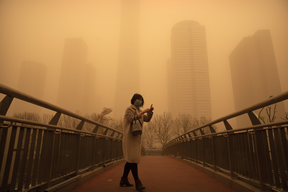 A woman walks along a pedestrian bridge amid a sandstorm during morning rush hour in the central business district in Beijing, March 15, 2021. Mark Schiefelbein via People Visual