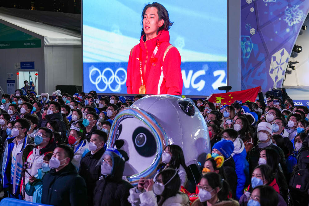 Olympic mascot Bing Dwen Dwen watches China’s Su Yiming receive a gold medal for Men’s Snowboard Big Air among a crowd, Beijing, Feb. 15, 2022. VCG