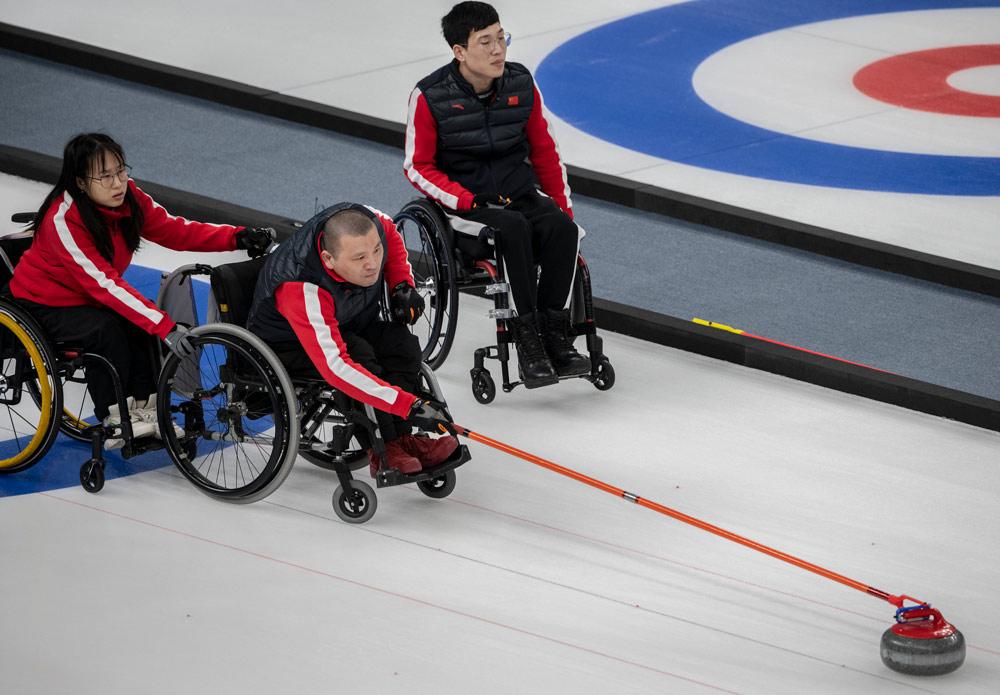 Chinese curler Shao Shengping (center) slides a rock as teammate Yan Zhou assists and Chen Jianxin (right) looks on during the wheelchair curling test event for the Beijing 2022 Winter Paralympics at the Ice Cube in Beijing, April 9, 2021. Kevin Frayer/Getty Images via VCG