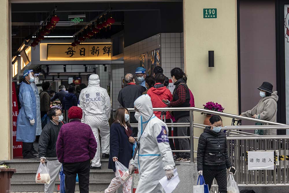 A police officer wearing personal protective equipment guards as residents queue to enter a food market in Shanghai, March 28, 2022. Shen Qilai Shen/Bloomberg via Getty Images/VCG