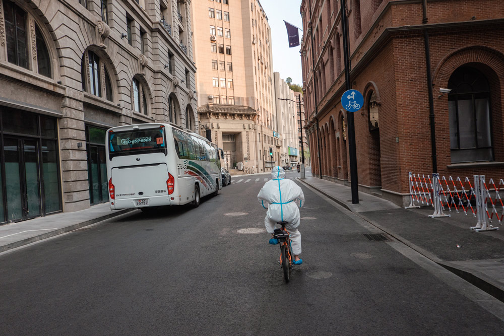 A worker in hazmat suit rides a rental bike in Shanghai, April 12, 2022. Gao Zheng for Sixth Tone