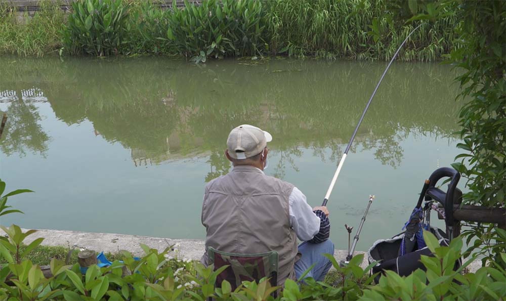 Mr. Wang fishes in the Xinjing River, Changning District, Shanghai, May 23, 2022. Chen Si/Sixth Tone