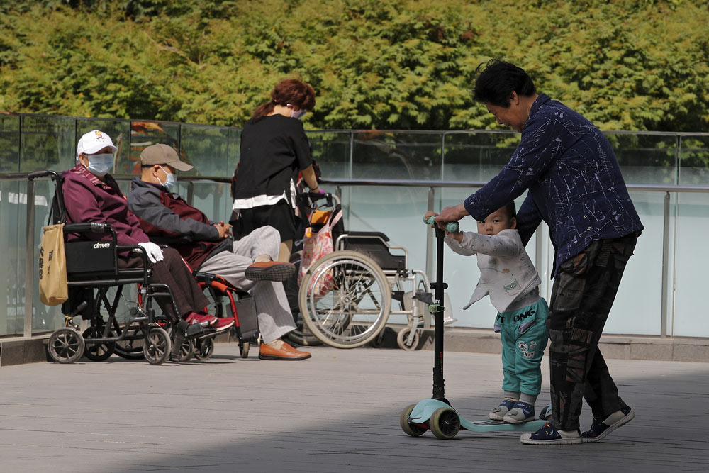 A woman helps a child ride a scooter outside a commercial office building in Beijing, May 10, 2021. Andy Wong/AP via VCG