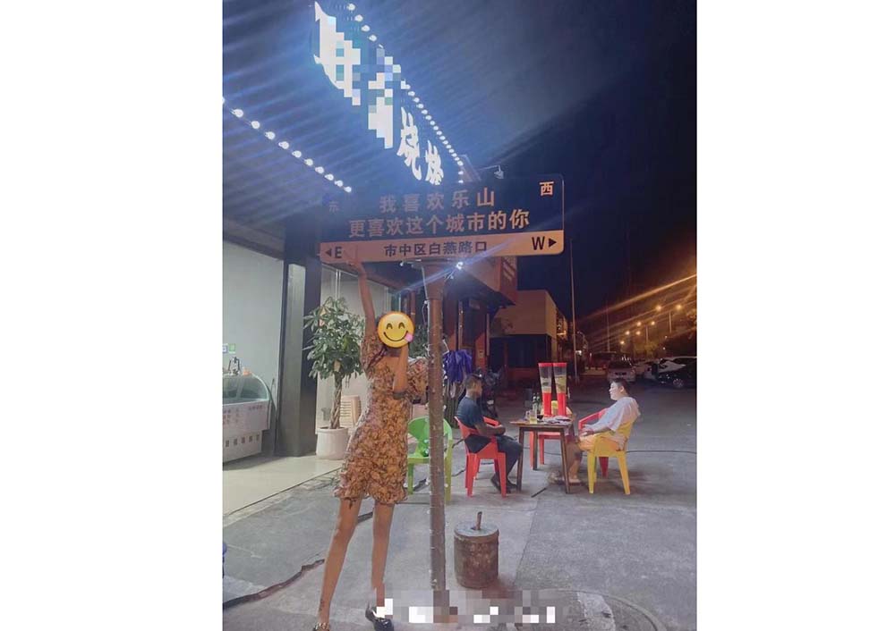 A woman takes photos by an illegal road side in front of  a restaurant, Leshan, Sichuan province, 2022. From The Paper