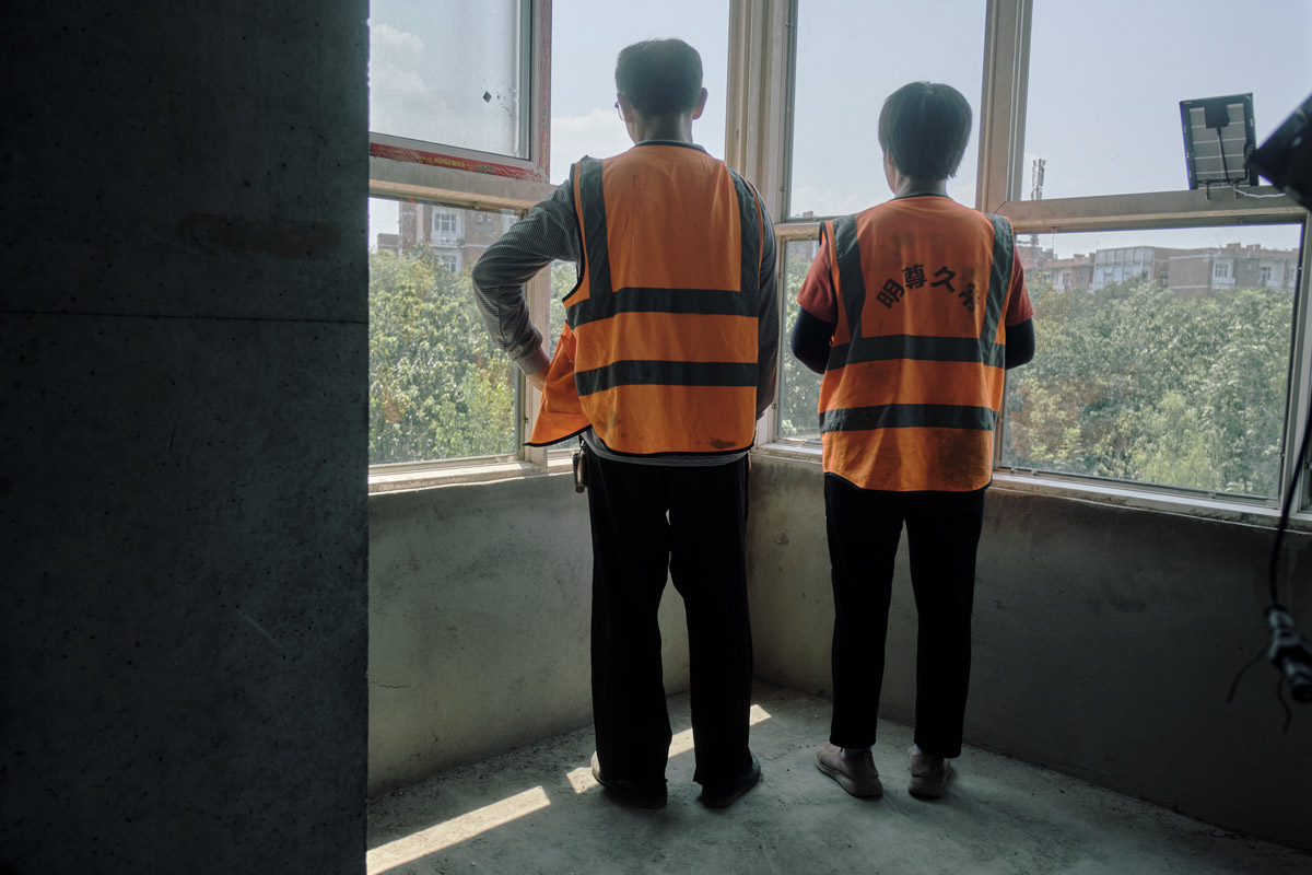 Wang Xudong (left) and Zhou Zongzhen (right) look out of their bedroom, August 2022. Wu Huiyuan/Sixth Tone