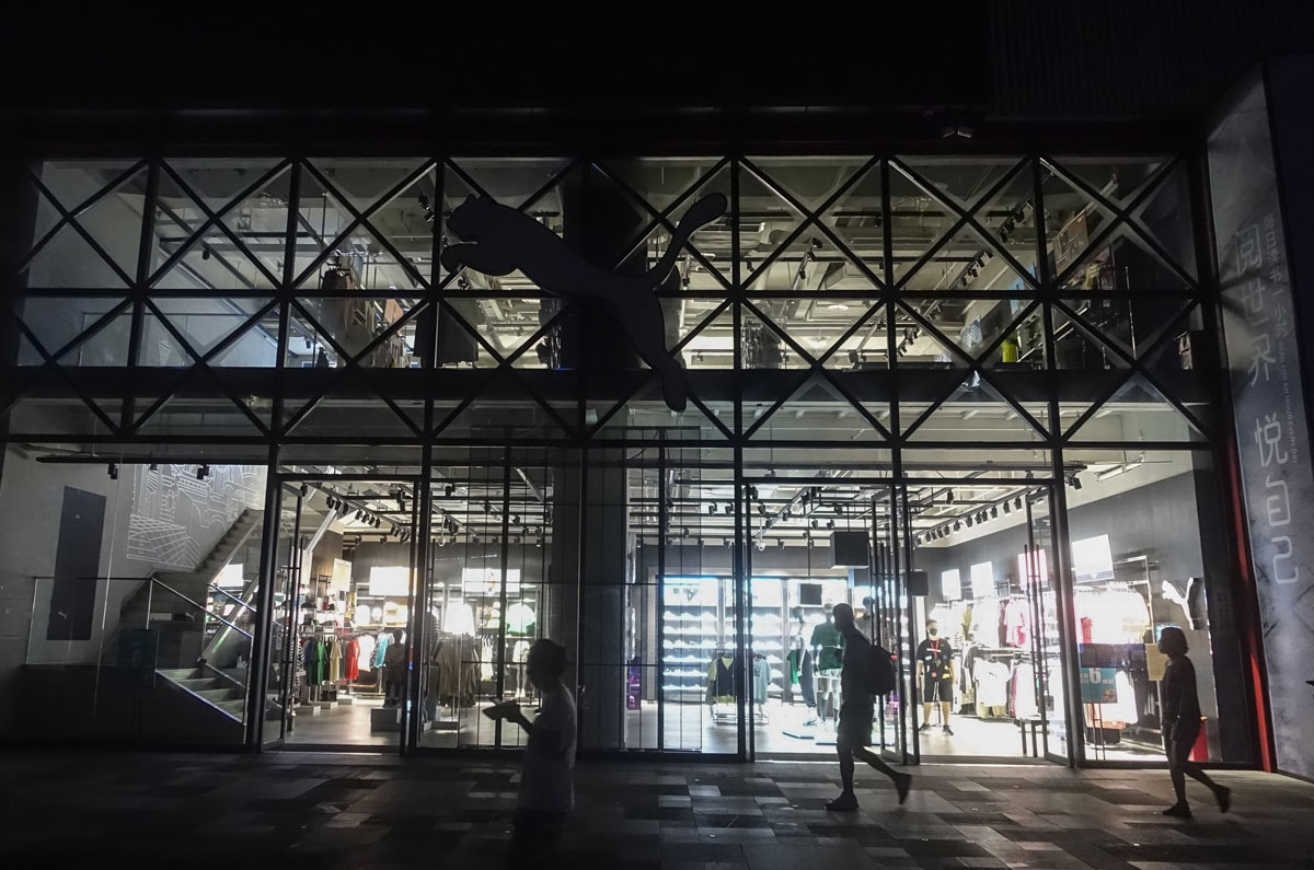 People walk past a Puma store, which has partly shut off its lights due to the local power-saving measures, in Chengdu, Sichuan province, Aug. 22, 2022. Yuan Kejia/IC