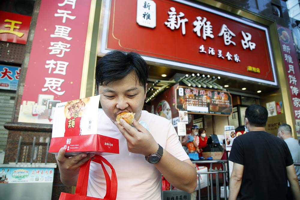 A man bits into a meat mooncake in front of a famous dessert house on the day of Mid-Autumn Festival in Shanghai, Sept. 10, 2022. Tang Yanjun/CNS/VCG