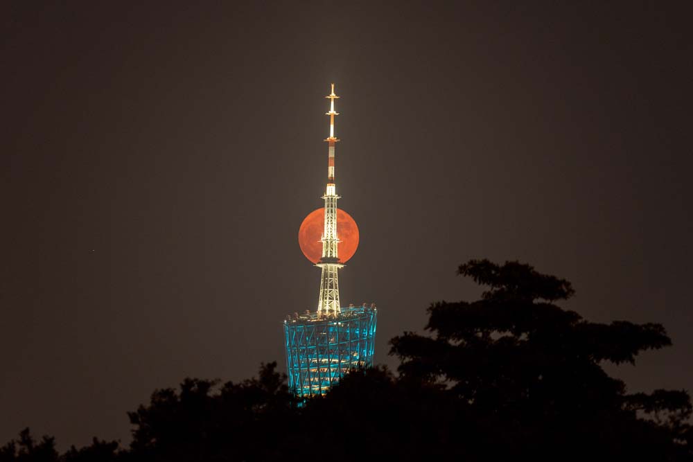 A full moon is seen behind the Canton Tower on the day of Mid-Autumn Festival, in Guangzhou, Guangdong province, Sept. 10, 2022. VCG
