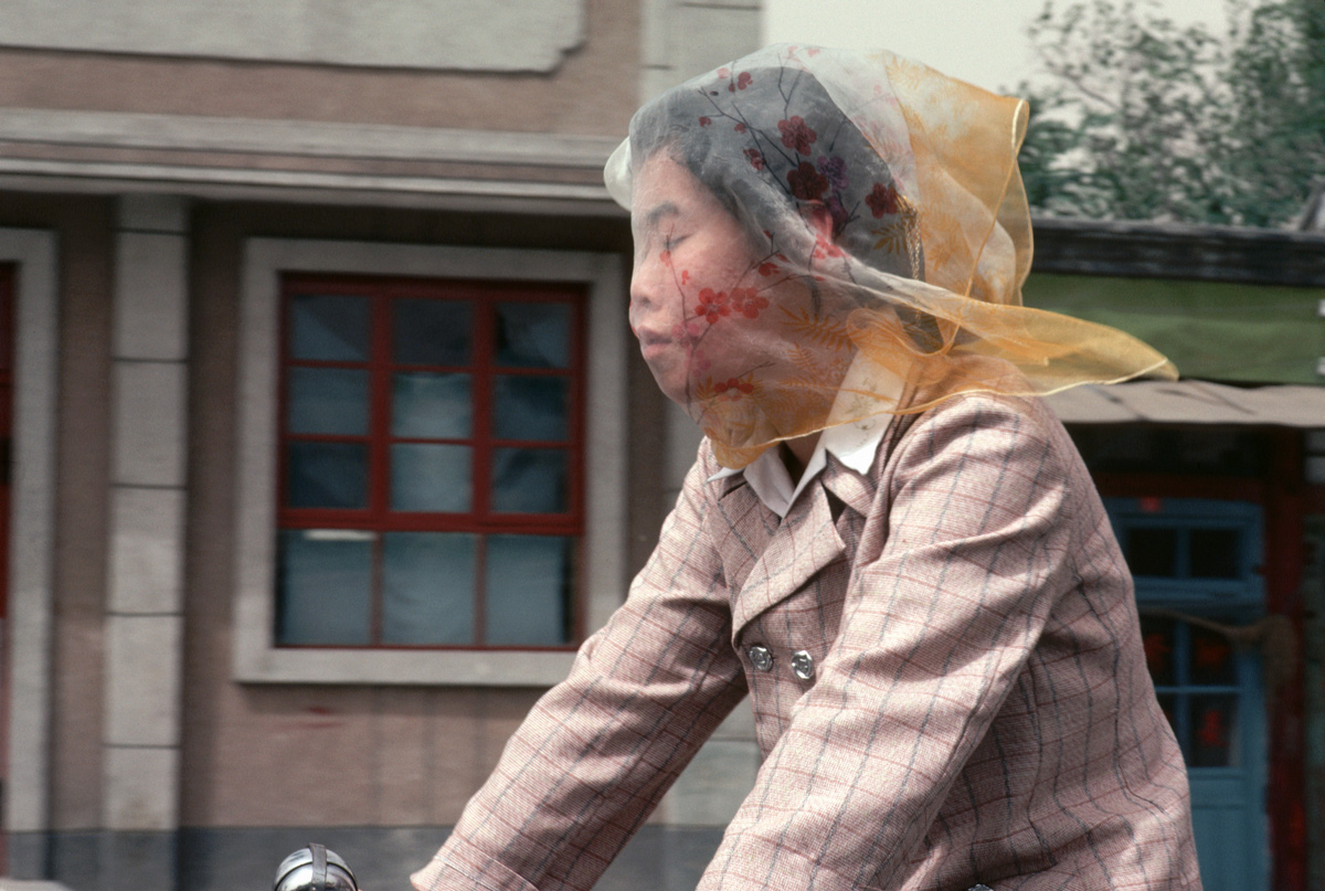 A student rides her bike to Peking University while wearing a veil to protect against the city's notorious dust storms, Beijing, 1981. Dean Conger/Corbis via VCG