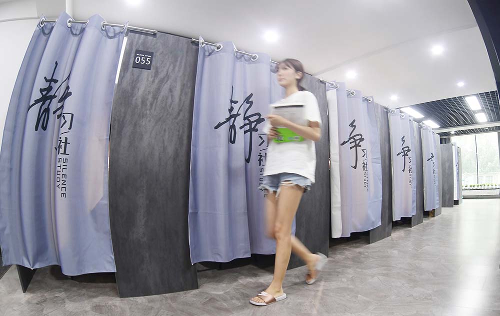 A woman holding books walks by study cubicles at a study room in Shenyang, Liaoning province, Aug. 12, 2020. VCG