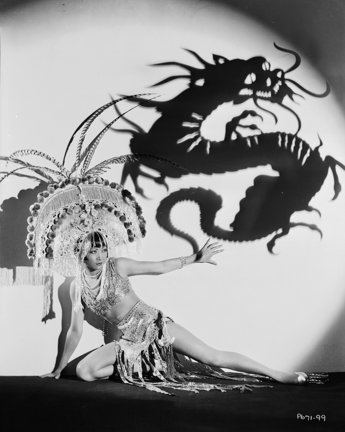 Anna May Wong wears an exotic costume and headdress, circa 1931. Above her is a projected shadow of a dragon. John Kobal Foundation via VCG