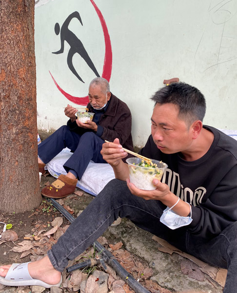 Luo Yong and his father eat a meal at a local primary school, 2022. The school was used as a temporary relocation site for affected families. Chen Canjie/The Paper