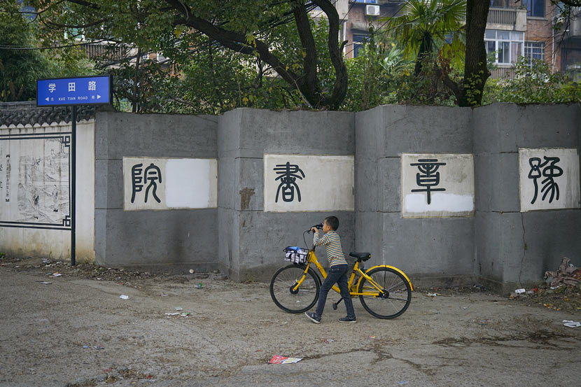 A child walks with a shared bike in front of the outer wall of Yuzhang Academy in Nanchang, Jiangxi province, Nov. 6, 2017. Yang Yifan/Caixin/VCG