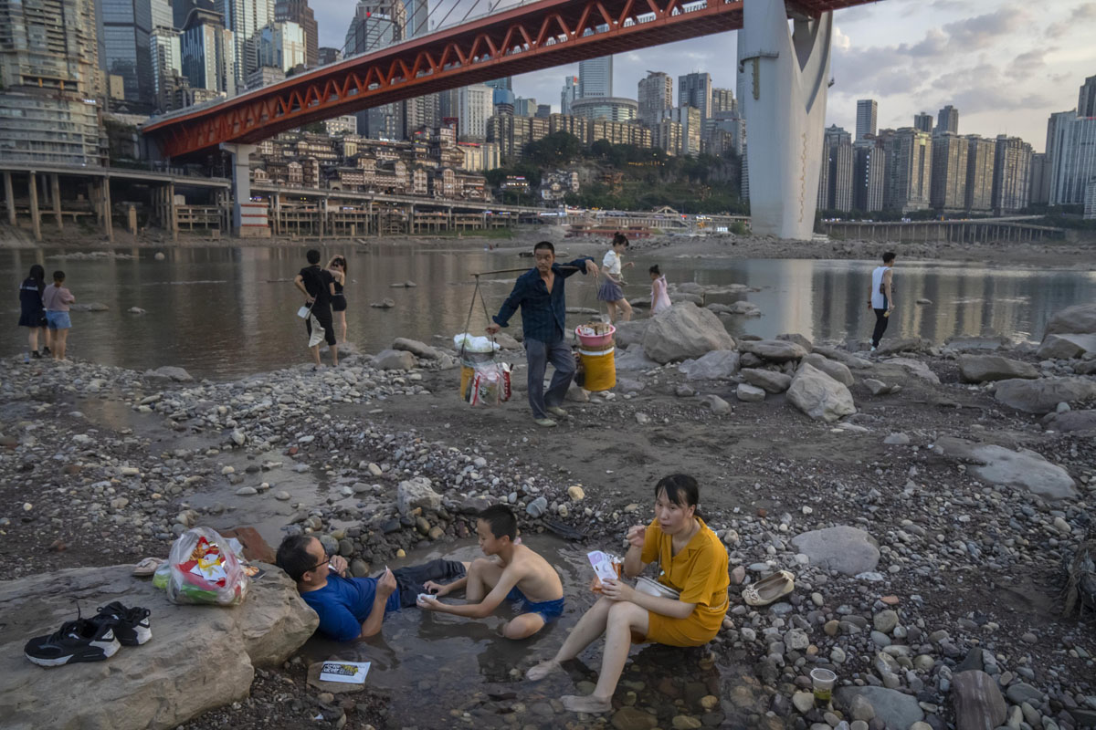 People sit in a shallow pool of water in the riverbed of the Jialing River, a tributary of the Yangtze, in Chongqing, Aug. 20, 2022. The very landscape of Chongqing, a megacity that also takes in surrounding farmland and steep and picturesque mountains, has been transformed by an unusually long and intense heat wave and an accompanying drought. Mark Schiefelbein/AP/VCG