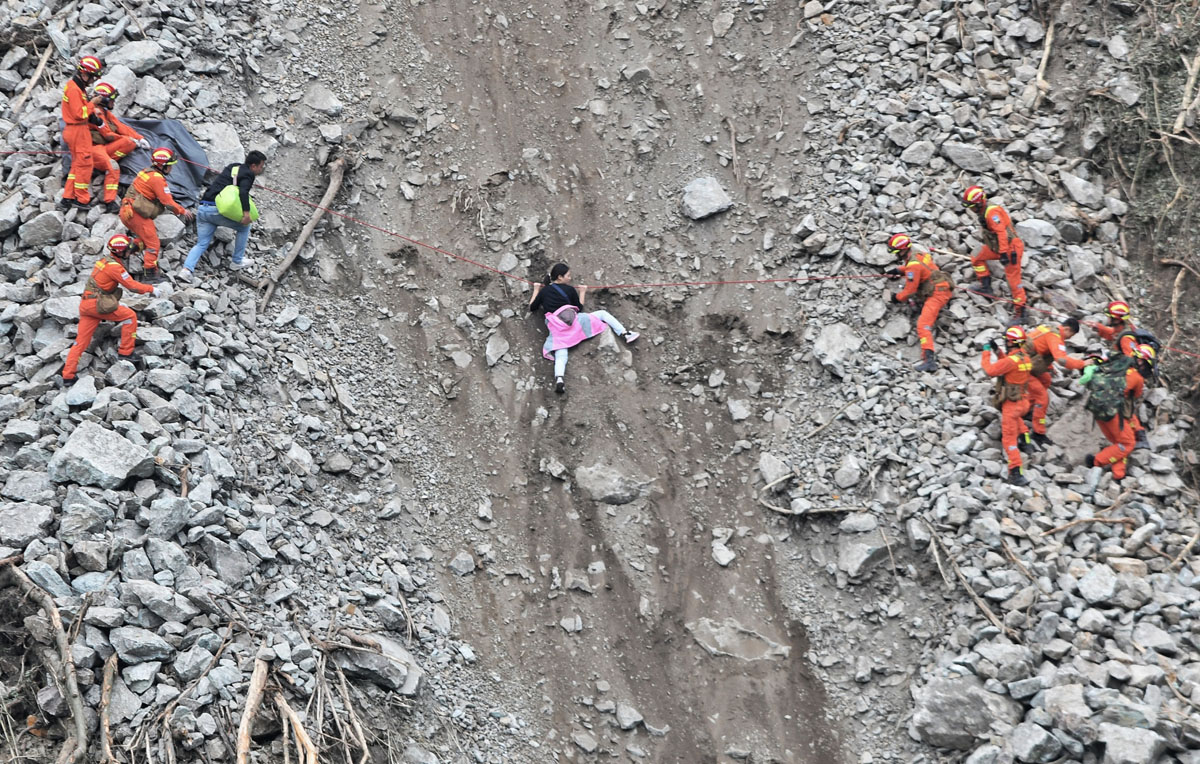 Rescuers help a woman cross a landslide in Ganzi Tibetan Autonomous Prefecture, Sichuan province, Sept. 6, 2022. The 6.8-magnitude Luding Earthquake killed at least 93 people, many of them in mountainous areas prone to landslides. VCG