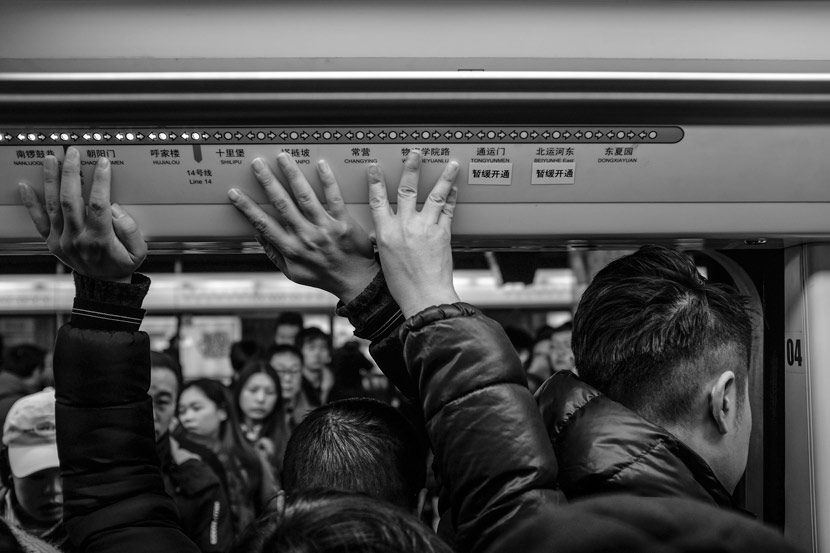 Passengers in a crowded subway car touch the ceiling for balance, Beijing, Dec. 26, 2017. Sun Kai for Sixth Tone