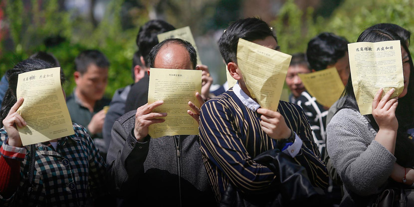 During police questioning, people participating in a pyramid scheme use leaflets to hide their faces from media photographers in Xi’an, Shaanxi province, March 31, 2016. Zhang Jie/VCG