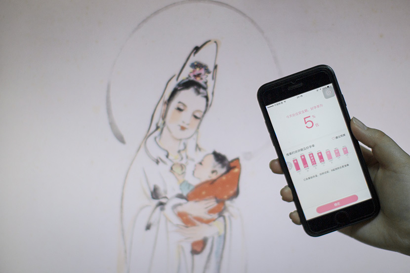 A woman uses pregnancy app Fengkuang Zaoren in Shanghai, Jan. 9, 2018. In the background is an image of the bodhisattva Guanyin, who is often associated with fertility. Shi Yangkun/Sixth Tone
