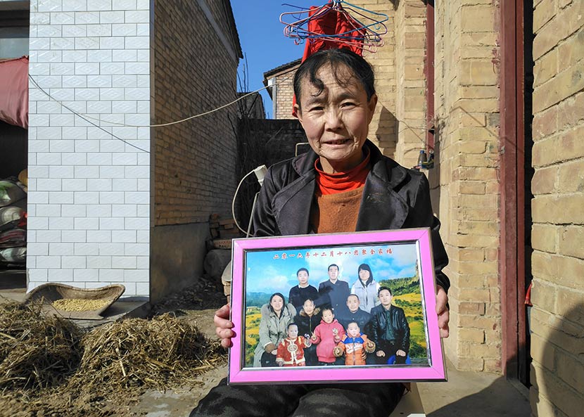 Li Xiaxia holds a family photo taken in December 2016, which includes her son Dong, near her house in Bin County, Shaanxi province, Nov. 7, 2017. Ming Que for Sixth Tone